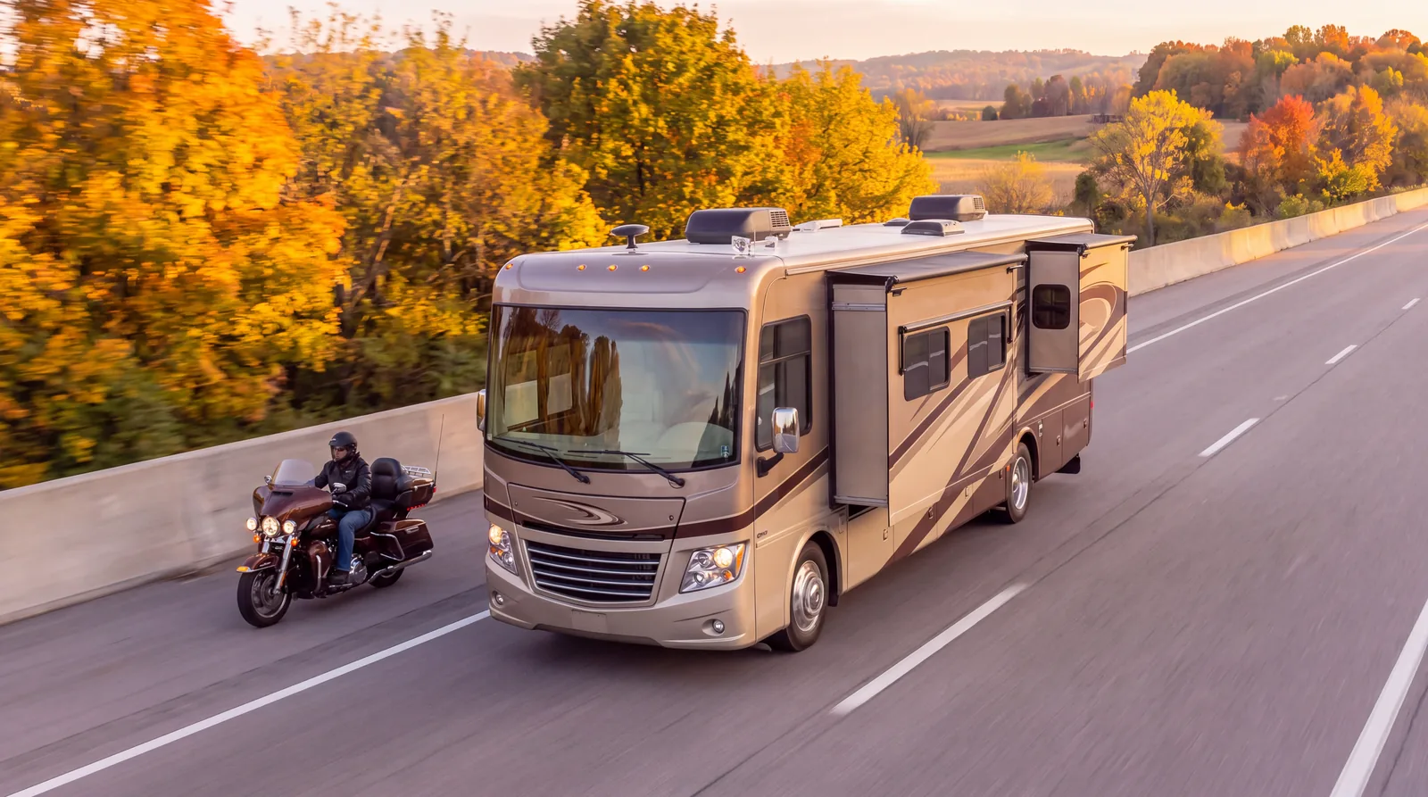An RV and a motorcycle on a highway lined with trees
